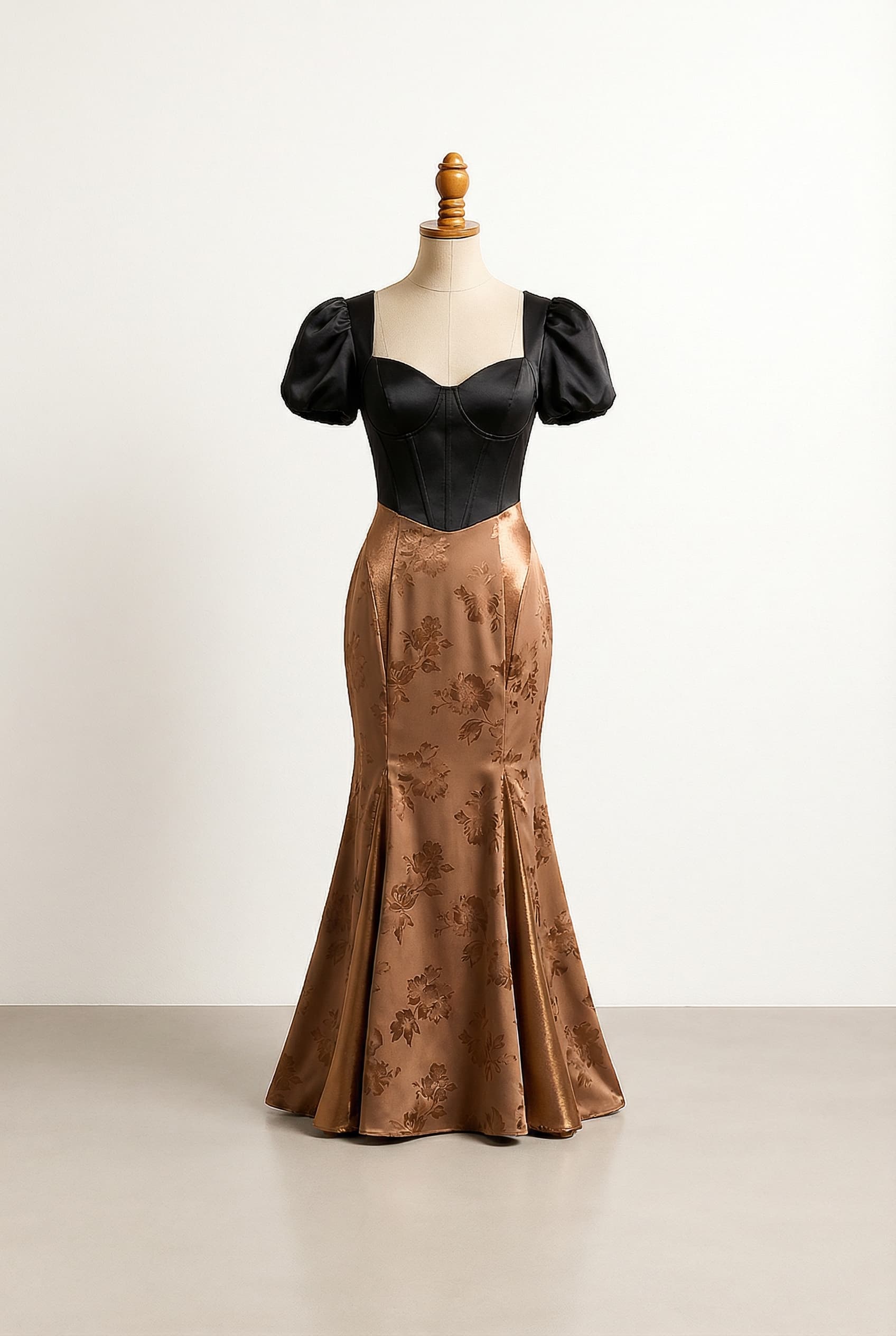 Glamorous prom dress with a Sweetheart neckline, a Satin black empire waist corset top with short puff sleeves, and a bronze patterned Mermaid bottom featuring a subtle flower print or polka dot with a matte finish and shiny bronze accents. The back features a zipper closure, with a large, solid bow in Black and bronze placed at the small of the back directly above the butt, matching the corset and extending down to form a train of a length that sweeps the ground elegantly, perfect for a prom without being too dramatic.