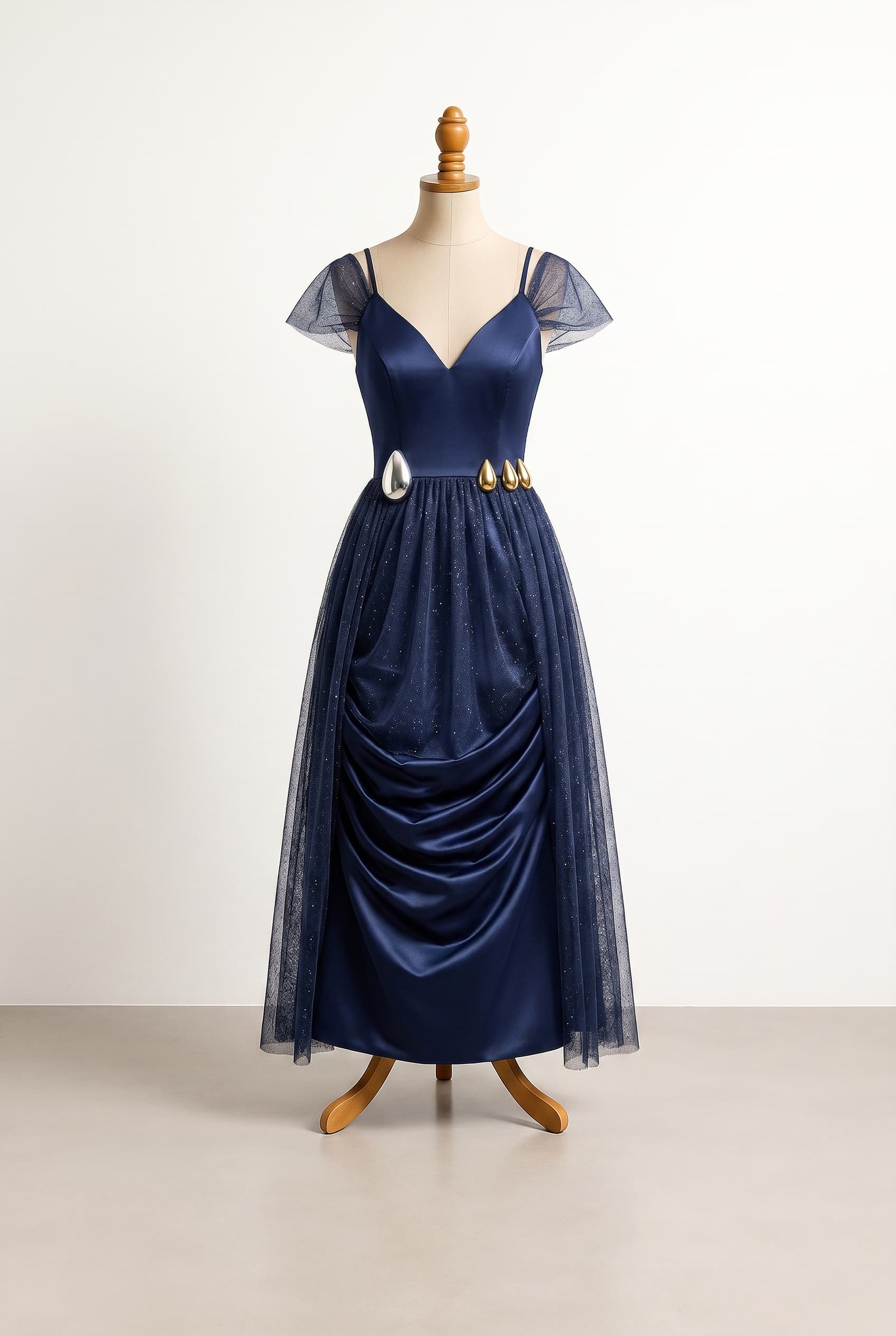 A balanced dress with a snatched waist featuring one plastic silver teardrop accent over half the waist and three smaller gold teardrops on the other side an ankle-length skirt featuring a V-neckline spaghetti straps and an over-the-shoulder overlay of sparkly navy mesh the bodice is plain navy featuring a skirt overlay of sparkly navy mesh that wraps fully around and the regular navy duchess satin underneath the mesh is ruched in the bottom area