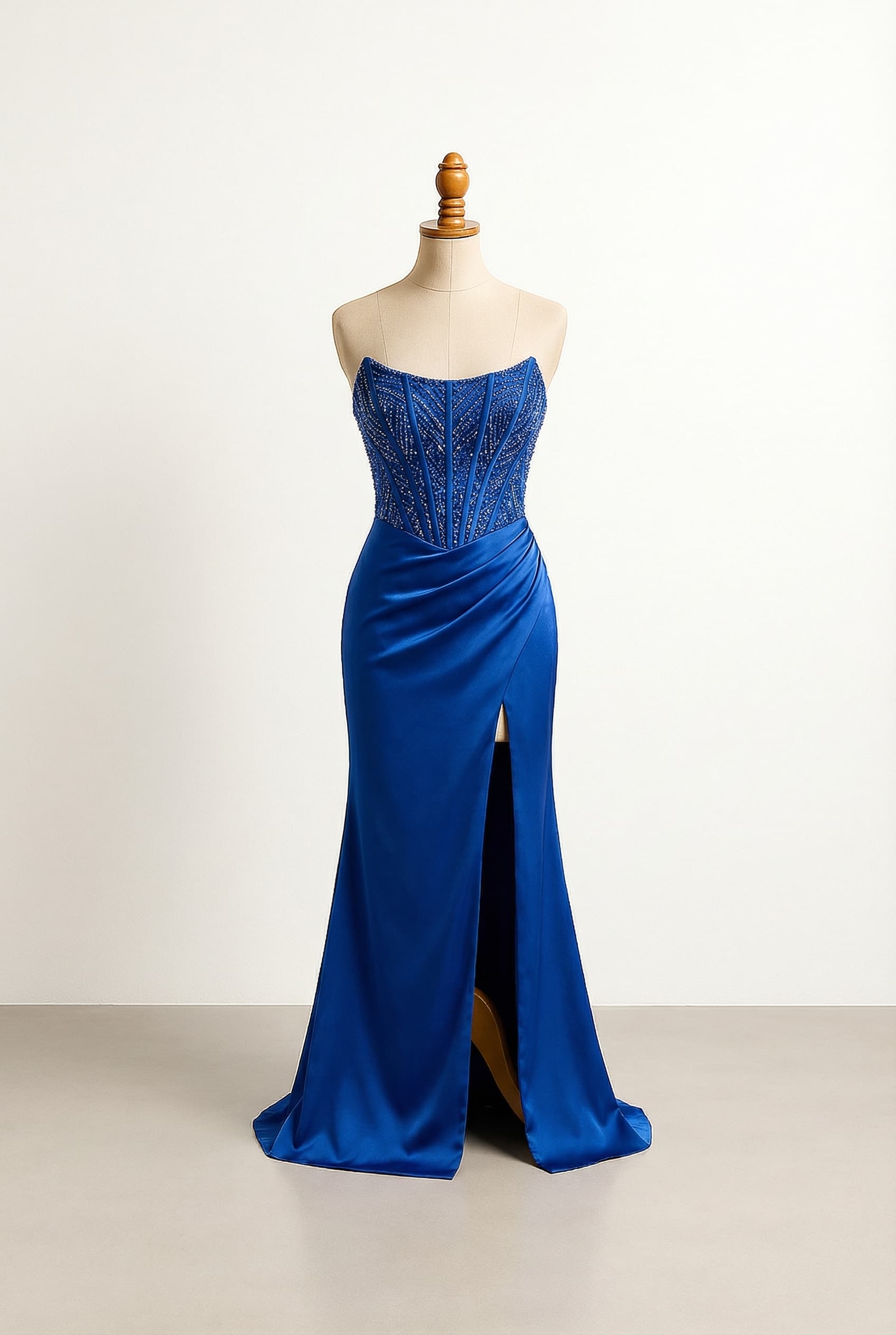 Glamorous floor-length form-fitting royal blue silk prom dress, strapless and sleeveless, featuring an asymmetrical corset, matching beading, and a high slit.