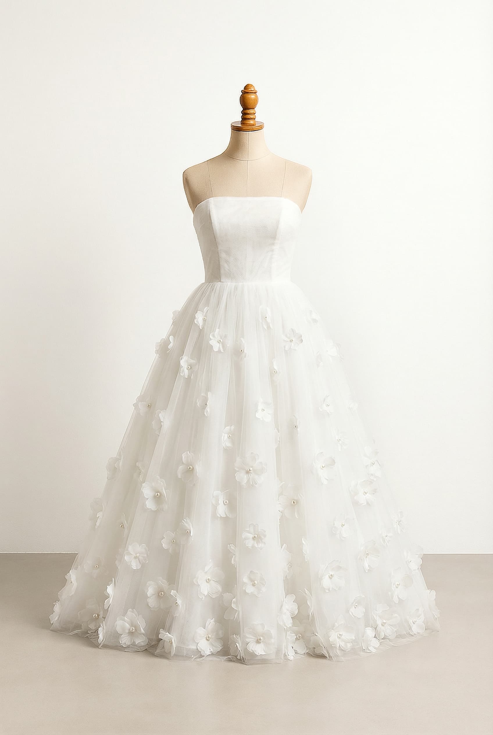 A romantic wedding dress with a strapless, intricately embroidered and beaded lace bodice, and a flowing tulle skirt adorned with flowers, each featuring a pearl in its center.