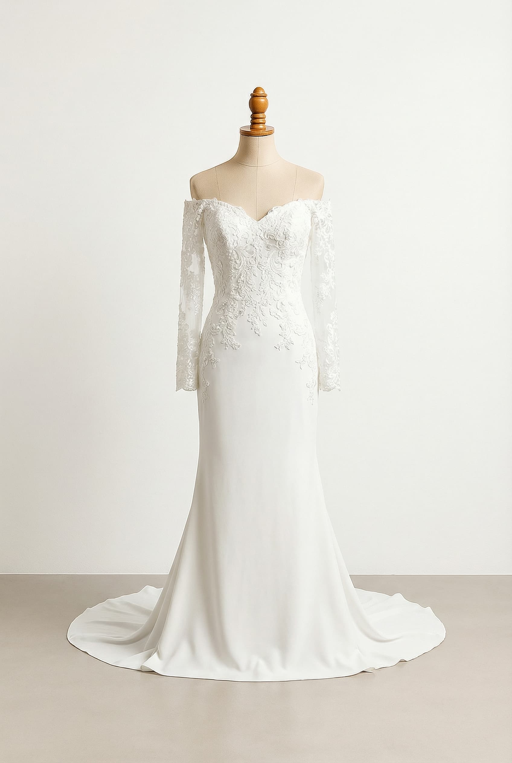 Wedding dress with an off-the-shoulder deep sweetheart neckline, fully covered lace appliqué long sleeves, a lace bodice concentrating on the bust and trailing onto a sleek, unbroken floor-length crepe skirt, and a sheath silhouette.