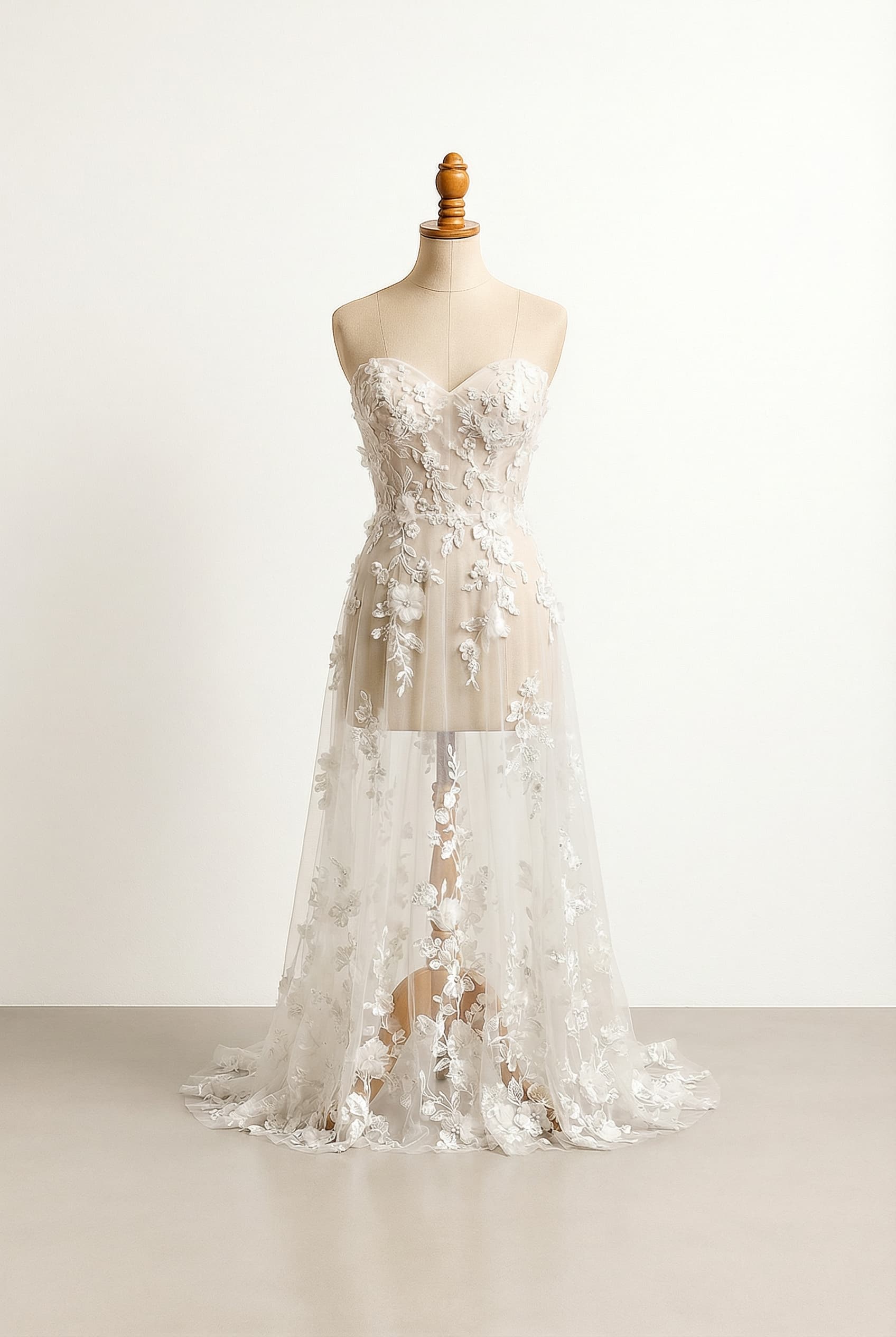 White wedding dress with a sweetheart neckline, fitted bodice, a sheer sheath overlay, adorned with scattered and trailing ethereal floral appliqués, creating an ethereal look.