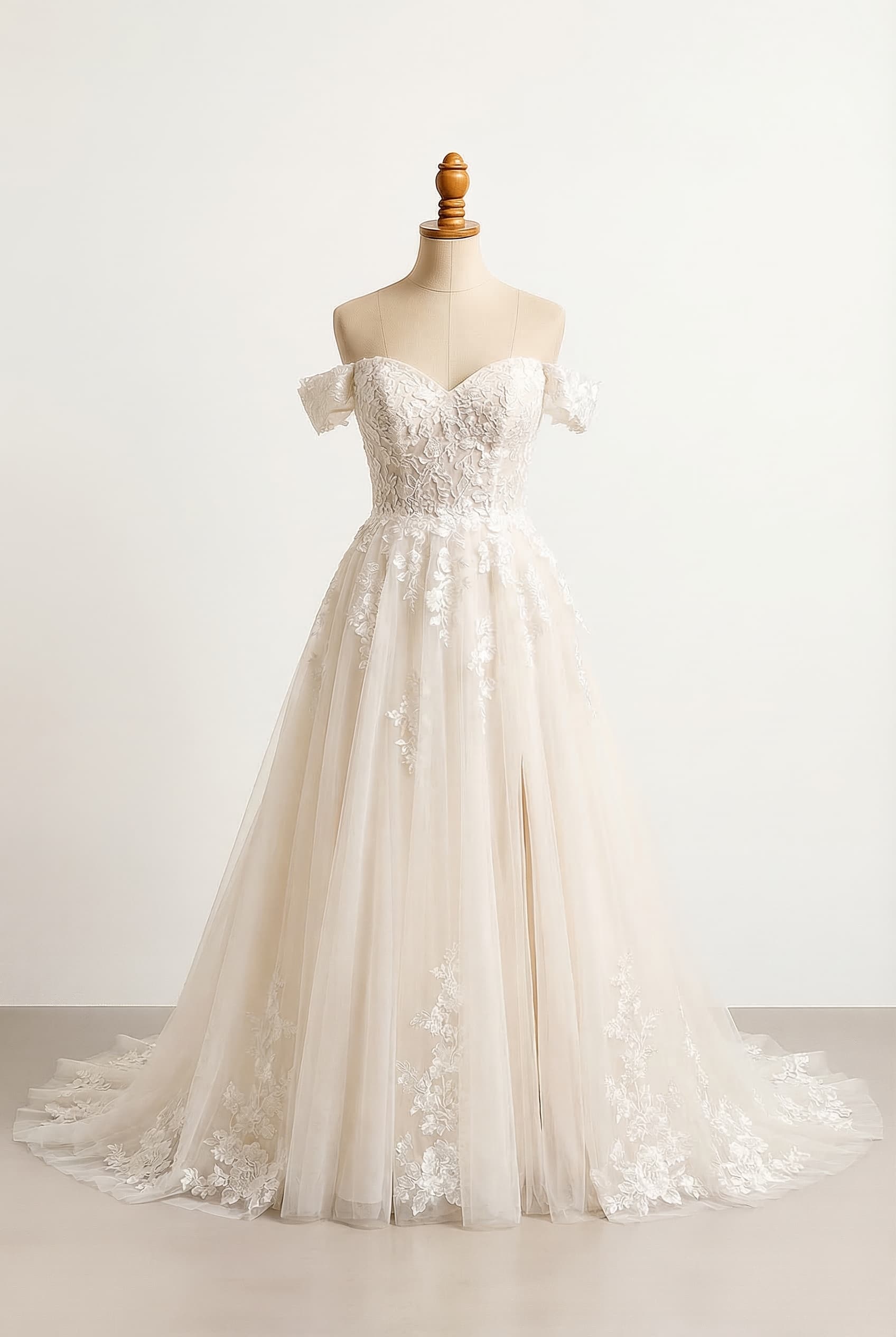 A-line ballgown with a very full tulle skirt high slit on one leg very light cream color sweetheart neckline off-the-shoulder sleeves structured and fitted bodice with floral lace appliqus concentrated at the top that gradually fade down into the skirt skirt made of multiple layers of soft tulle for volume with floral lace appliqus fading downward and larger floral lace details along the hem of the dress long flowing train floral lace details and a slit on the dress