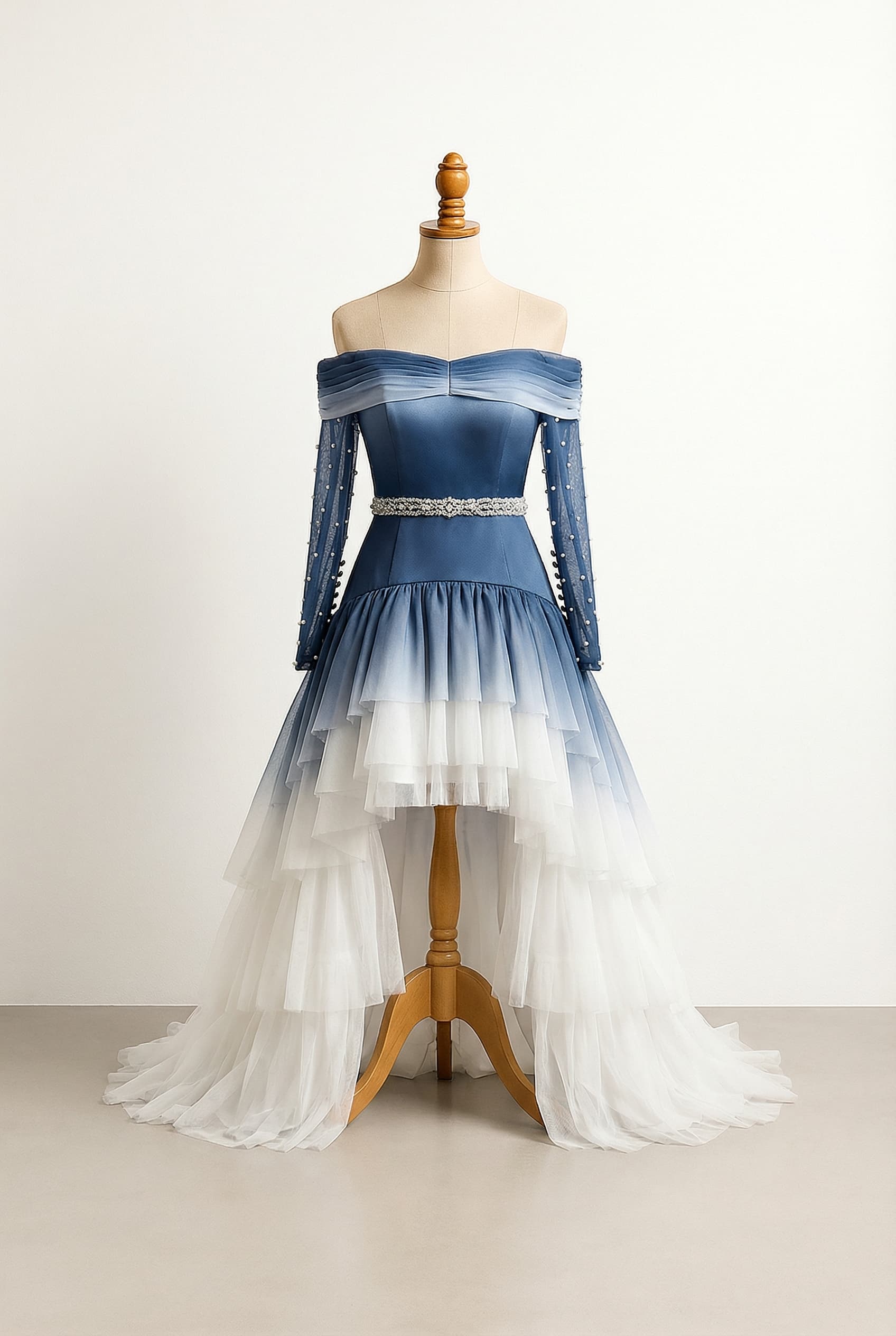 A romantic wedding dress with elegant details, featuring a gradient from dark blue to white, a high-low length with a removable outer skirt and multiple ruffled tiers, a low straight neckline, long pearled sleeves with a pleated chiffon off-shoulder wrap, a drop-waist silhouette, made with satin, chiffon, and tulle, a button-up back to mid-upper back, with lace applique on the back, pearl buttons on the sleeves, and a rhinestone and pearl sash.
