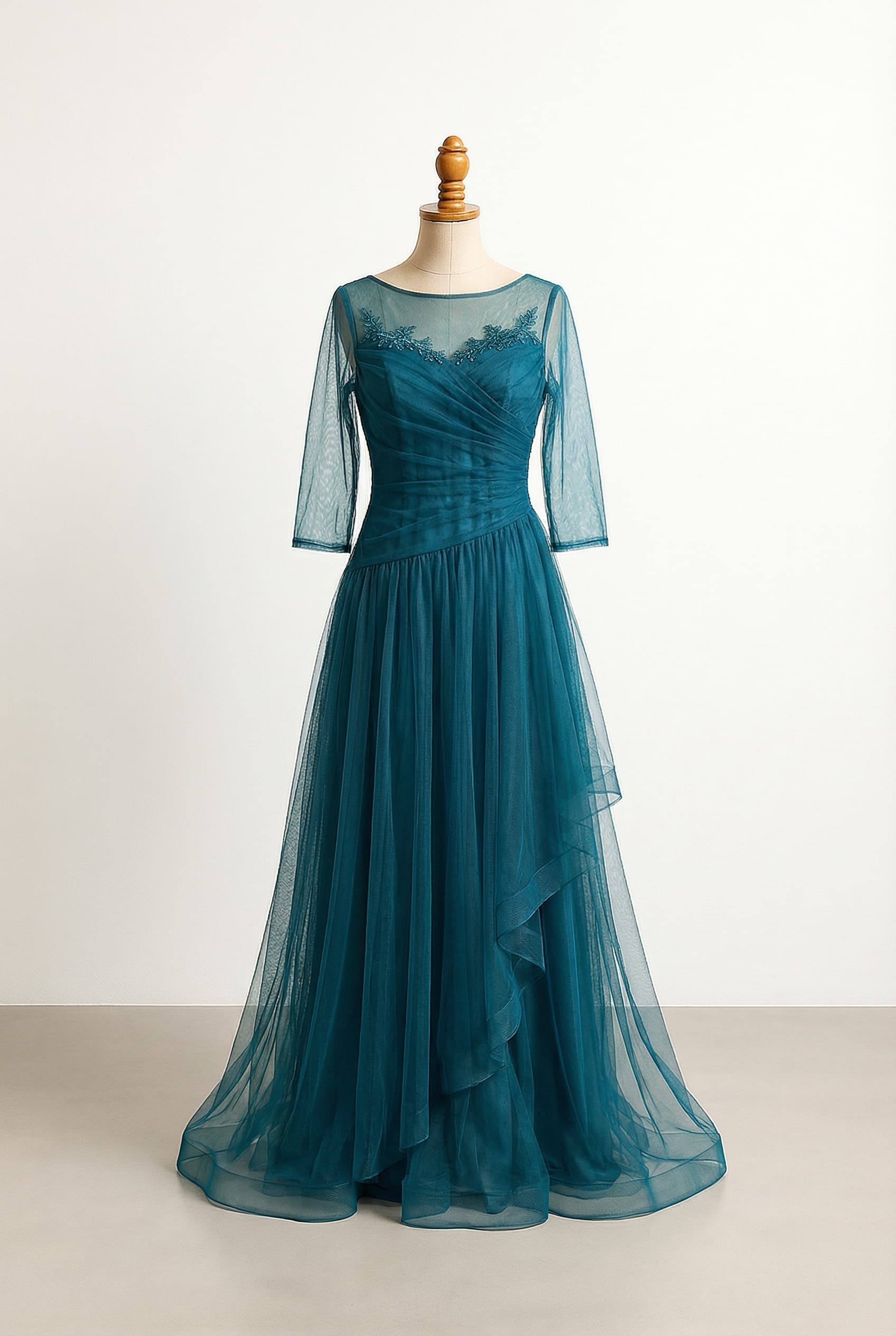 A-line flow floor length dress with modest or illusion neckline, drop waist, soft ruching, panels that float, gentle layering, and short sleeves or 3/4 length sleeves in peacock, deep teal, blue green, navy with teal tulle or net, or emerald softened by lighter teal tulle or net in blue green, soft peacock, muted green blue. The dress has movement and visual softness, floats without cling, and skims hips gently rather than clings. It has enough detail to distract the eye and create shape, with a pattern that isn’t too busy. It has an overlay and soft pleating.