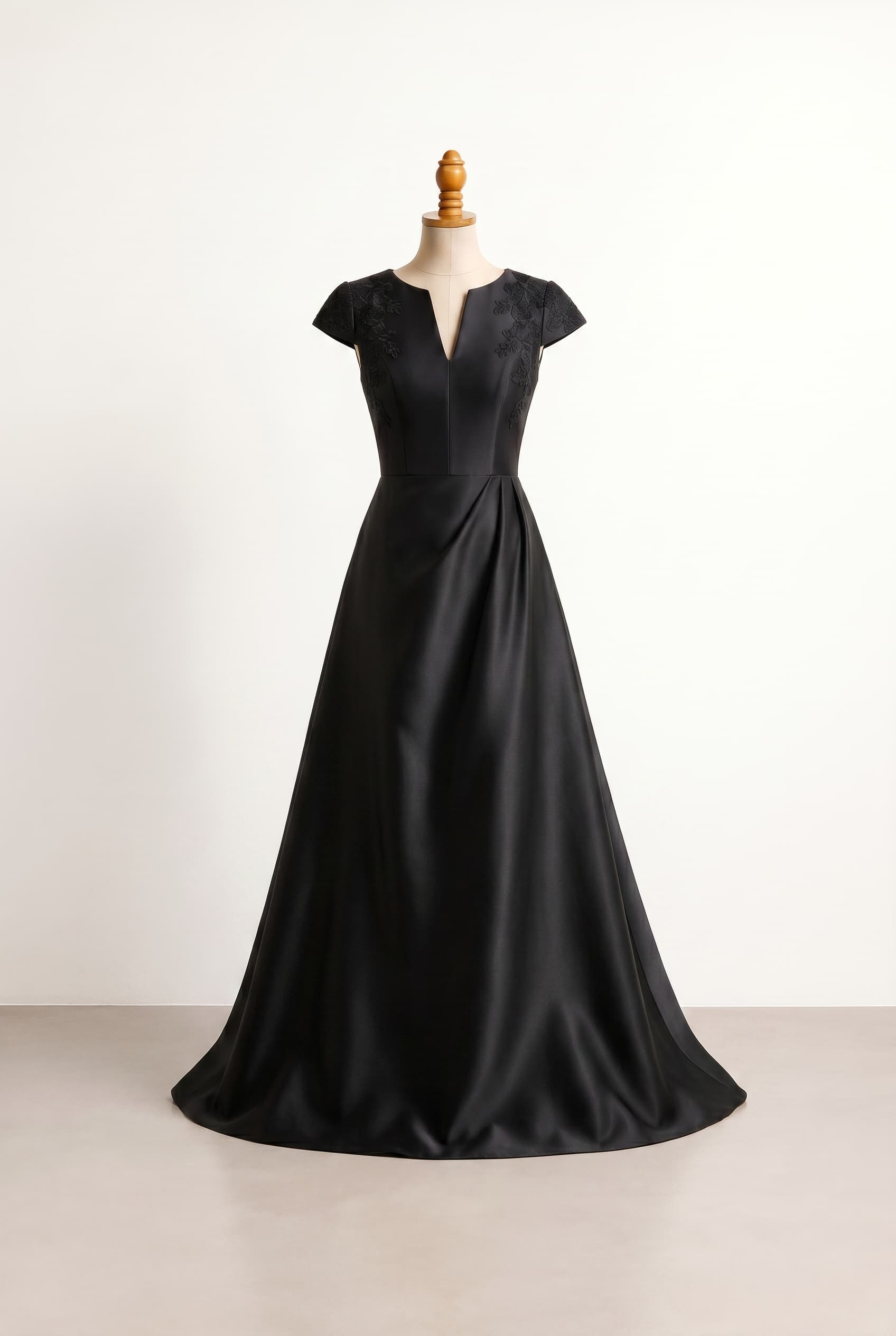 Modern A-line gown with black shorter cap sleeves featuring floral lace appliqu a subtle V-neckline a clean structured design a drape starting at the natural waistline and a more flowy flared floor-length hem