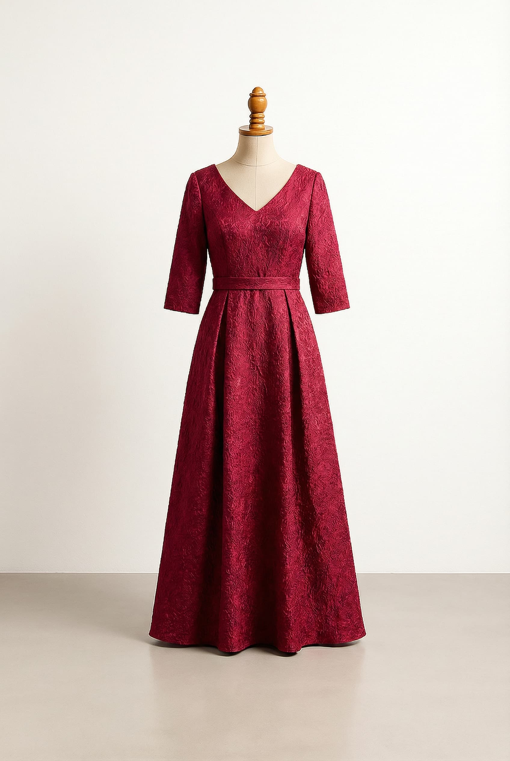 Red a-line floor length evening gown three-quarter sleeves v neck, with textured fabric and a belt.