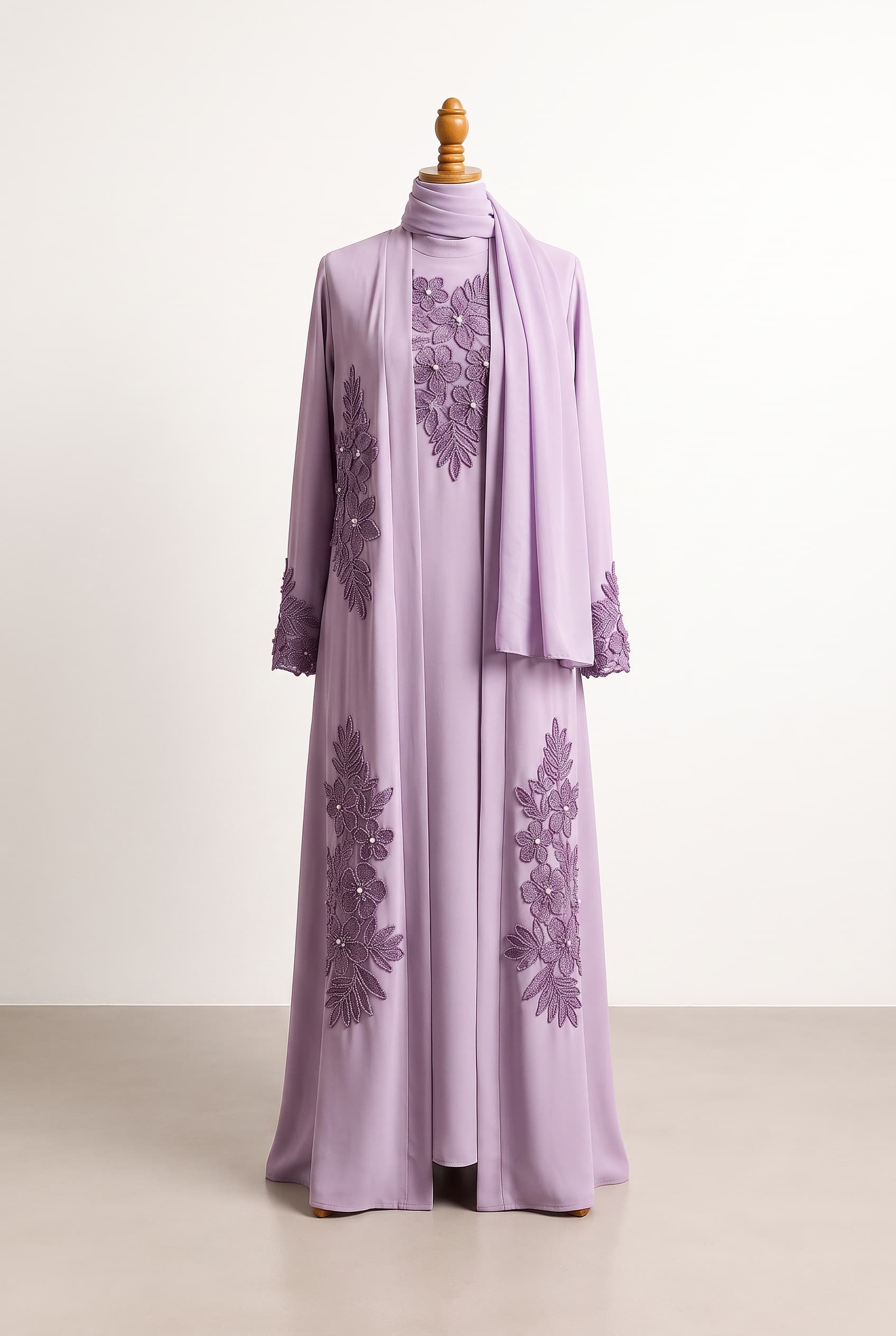 Three-piece modest lilac set consisting of a full-length straight-fit dress, open abaya, and chiffon scarf. Dress and abaya in medium-lightweight matte crepe georgette, 100% opaque. Dress has a plain lilac mock neck, long fitted sleeves, and darker-lilac 3D tropical floral lace on the chest and sleeve cuffs. Matching open abaya has long fitted sleeves with darker-lilac 3D tropical floral lace on both left and right front sides, sleeve cuffs, and the lower back. Floral design uses varied-size tropical lilac flowers and leaves, each outlined with tiny beads and each flower centered with one tiny pearl. No zippers, glitter, or sequins; any nighttime sparkle comes only from the bead and pearl detailing.; clean front line, elegant movement, and refined restraint