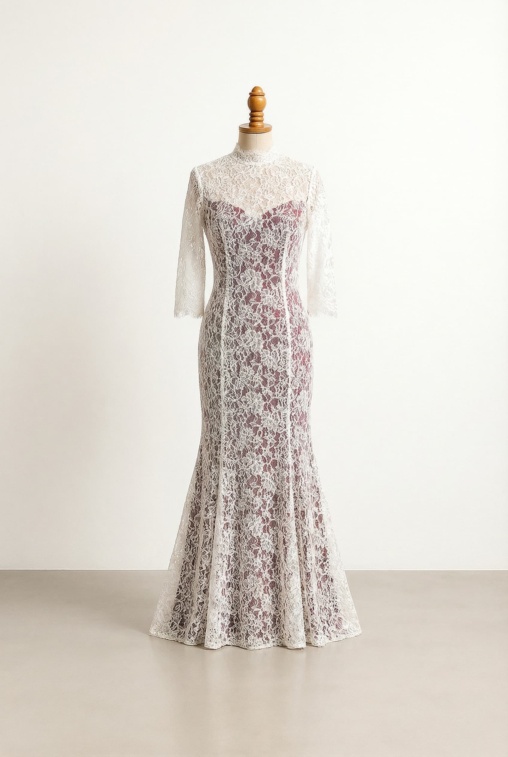 A white lace wedding dress with burgundy peeking through the lace, high neck, three-quarter sleeves, and a mermaid silhouette.